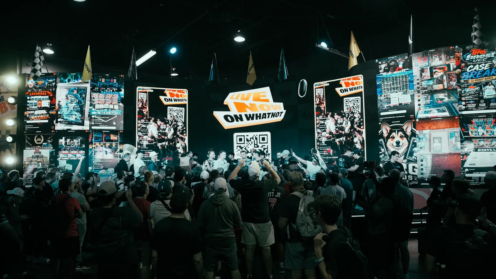 A crowd several deep in front of the Whatnot stage at The National, phones raised, a wall of live-stream screens and a LIVE NOW ON WHATNOT sign above the breakers